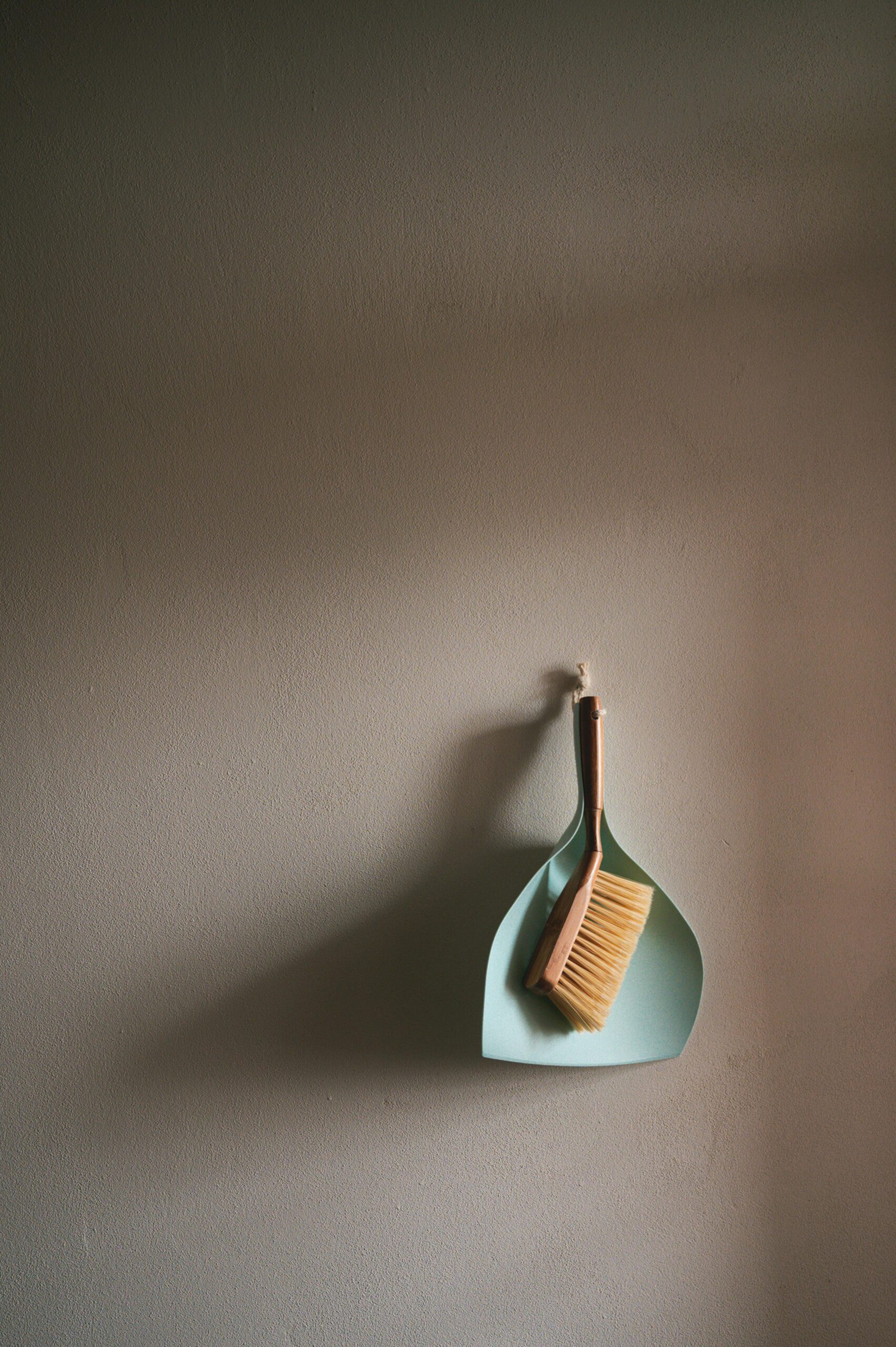 A simple dustpan and brush set hanging against a clean grey wall, perfect for cleaning concepts.